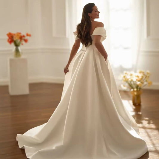 Woman in a white off-shoulder wedding dress standing in a bright room with flowers.