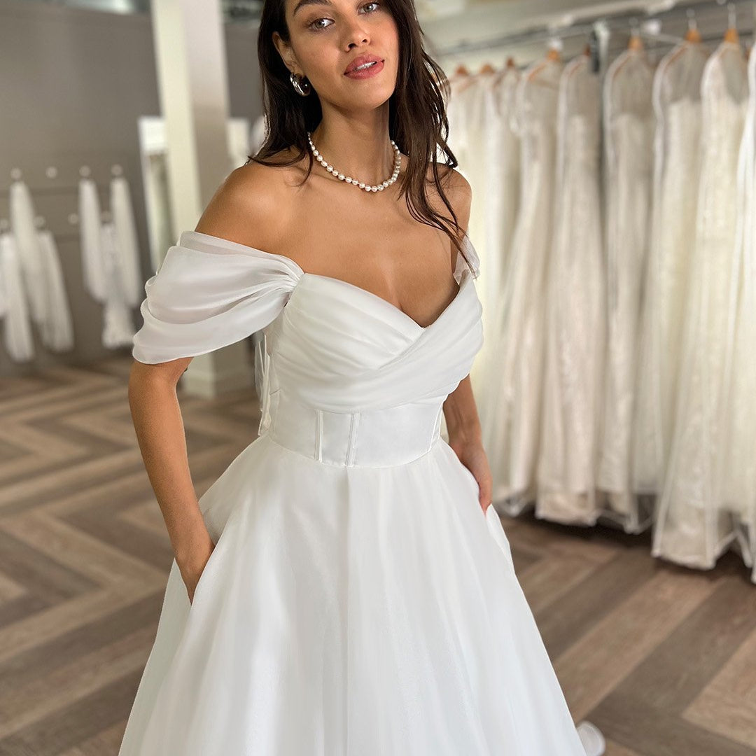 white a-line off the shoulder organza fabric wedding gown with side pockets and satin underskirt