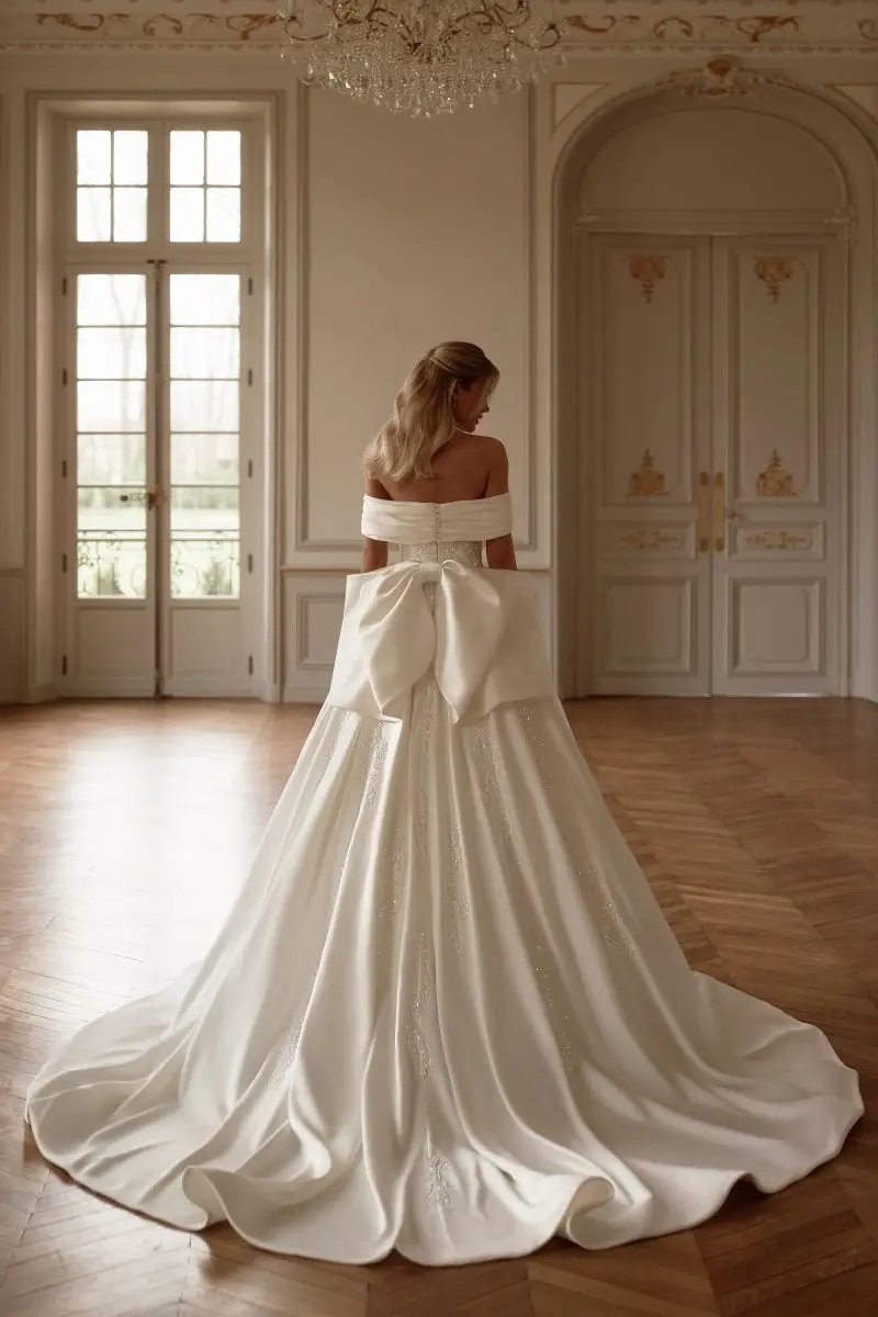 Satin wedding dress has an off the shoulder design with a large back bow and court train sizes 2-26w