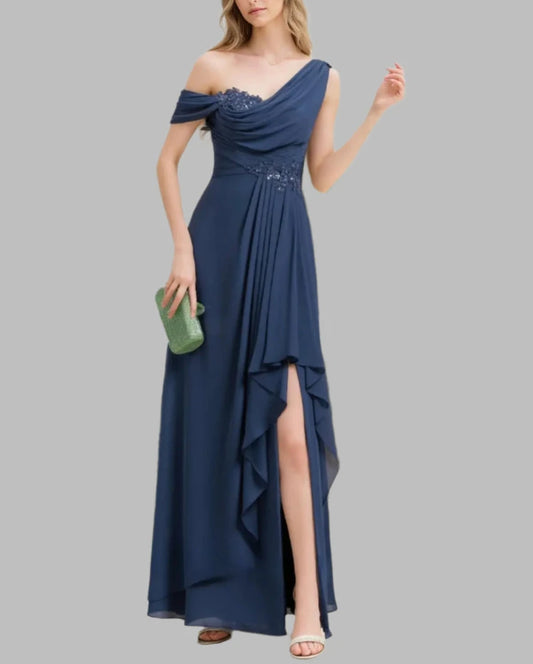 Woman wearing a blue off-shoulder dress with a slit, holding a green clutch, against a white background with greenery.