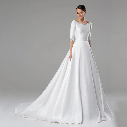 A woman wearing a white, satin A-line wedding dress with half sleeves, a scoop neckline, and a sweep/brush train.