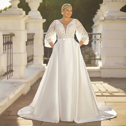 White satin wedding dress with lace long sleeves, V-neck, and belted waist