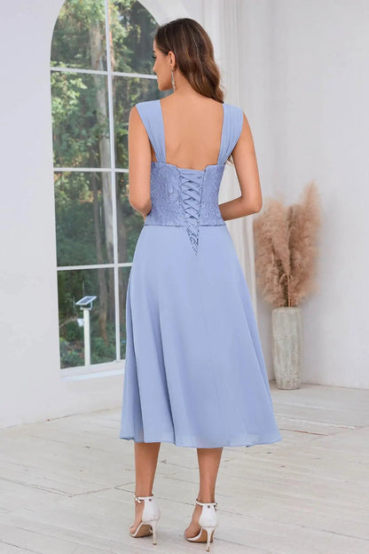 Woman wearing a light blue dress with a corset back, standing in a room with a large window and decorative plants.