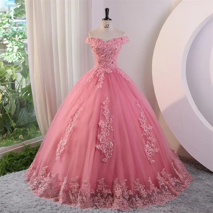 A pink off-the-shoulder applique lace luxury ball gown with a floor-length skirt, displayed in a room with draped curtains.